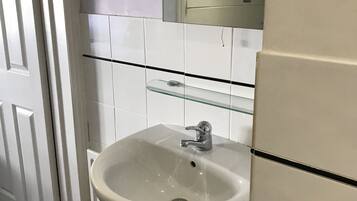 Un baño con un lavamanos blanco, un espejo y una repisa de vidrio arriba.