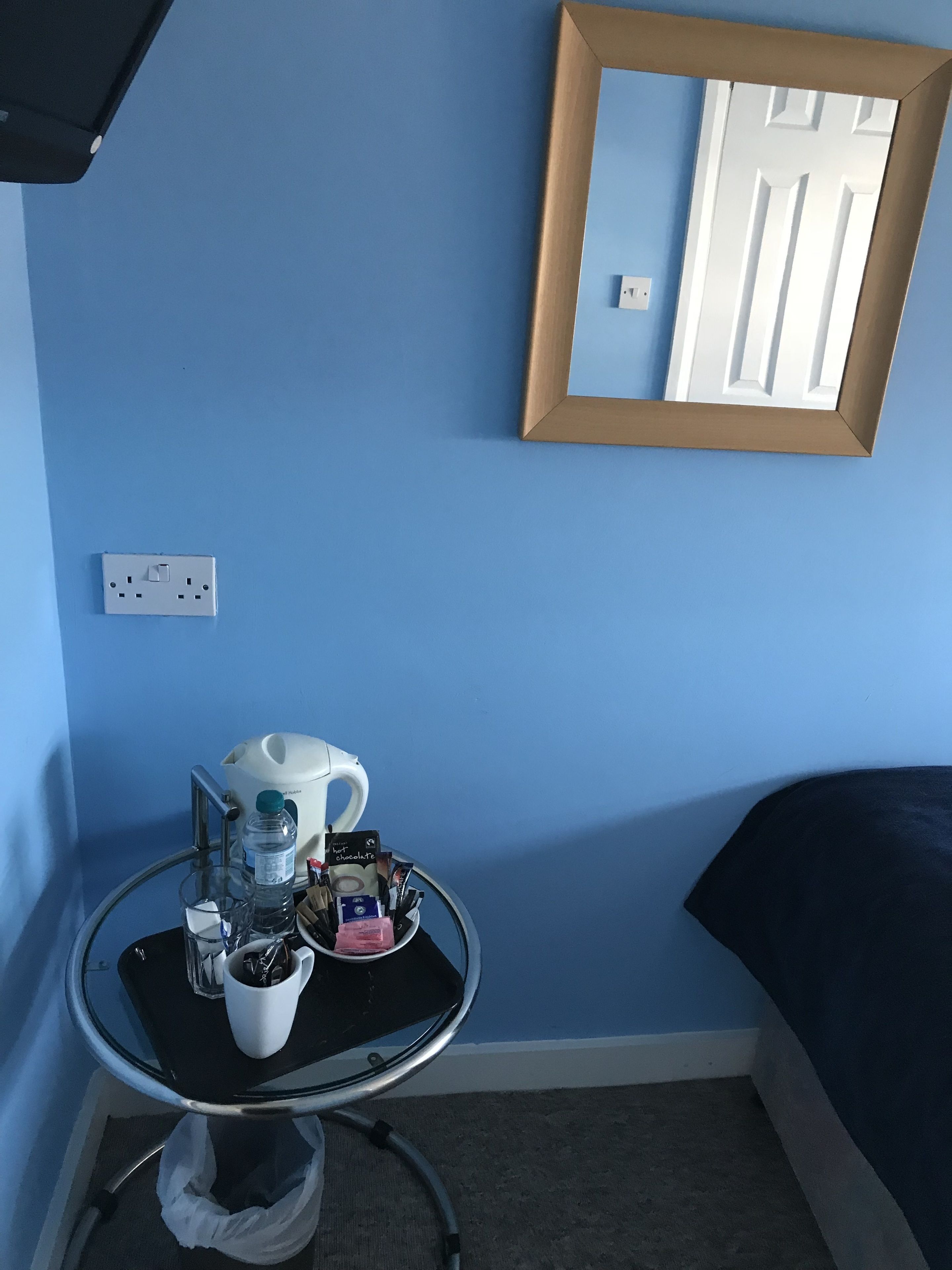 A small room with a blue wall, a round table with a coffee cup, a water bottle, and a mirror.