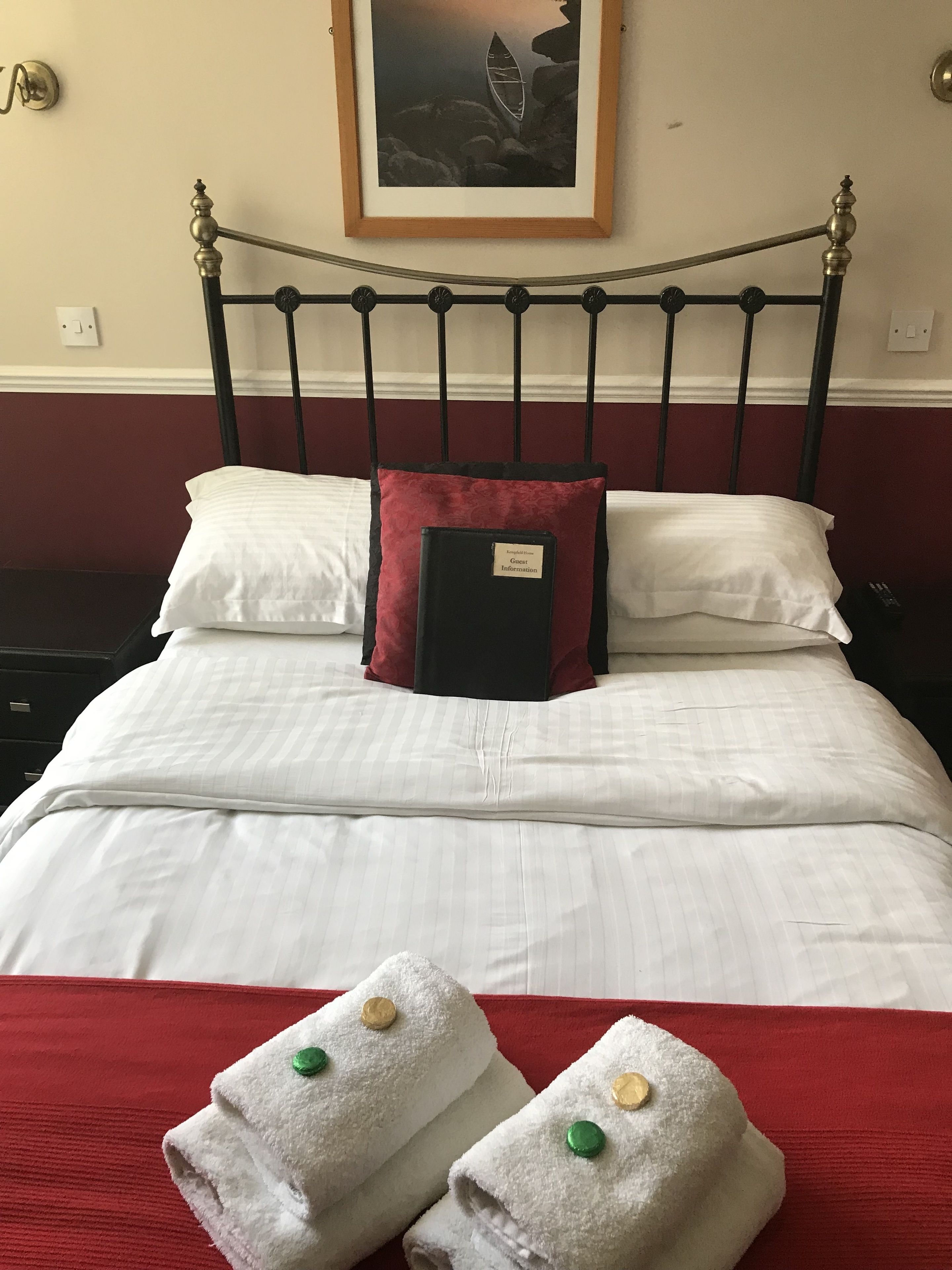 A neatly made bed with white linens, a red pillow, and a black book titled "Guest Information" on the headboard.