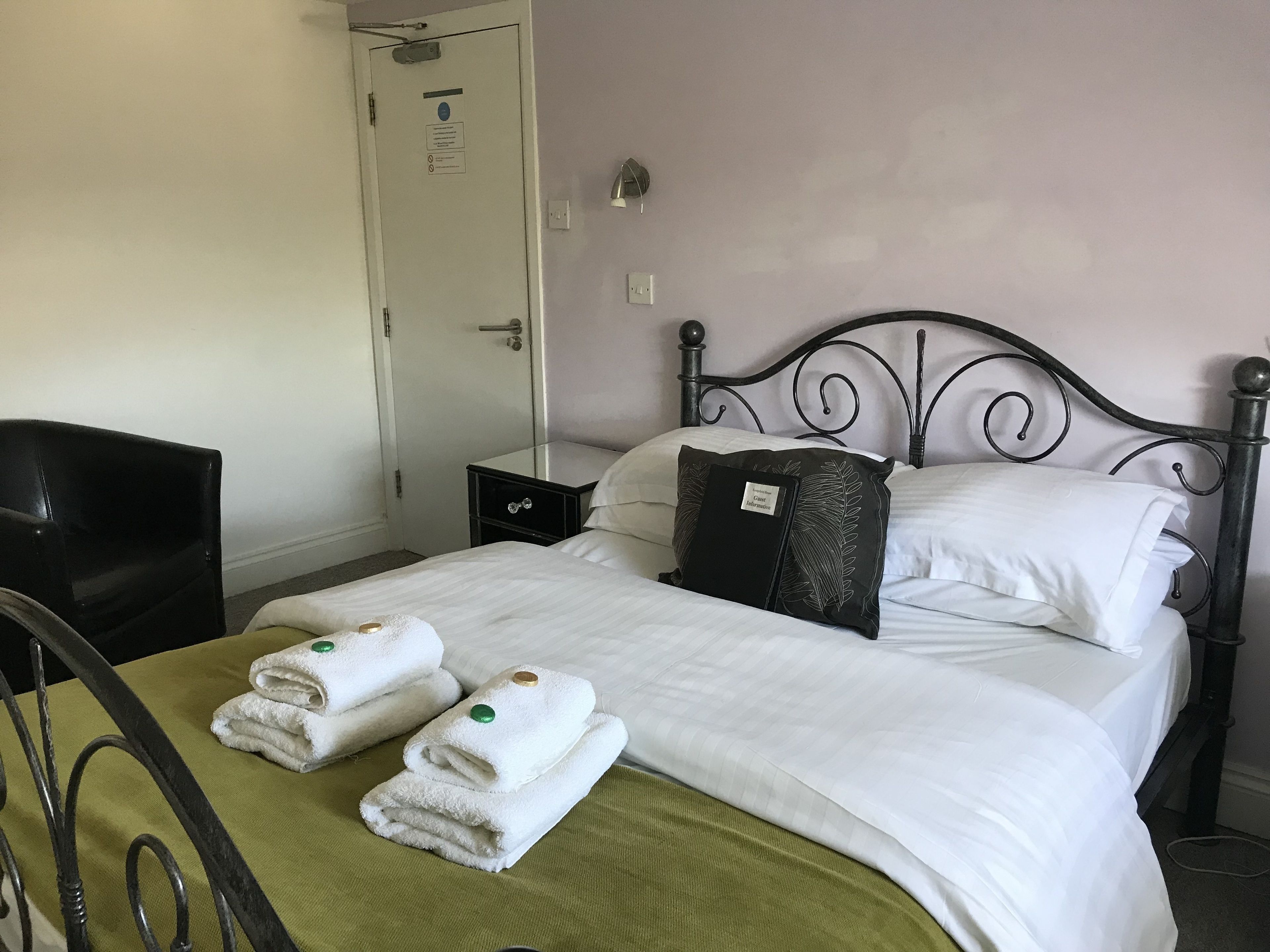 A neatly made bed with white linens and two folded towels on a green bedspread.