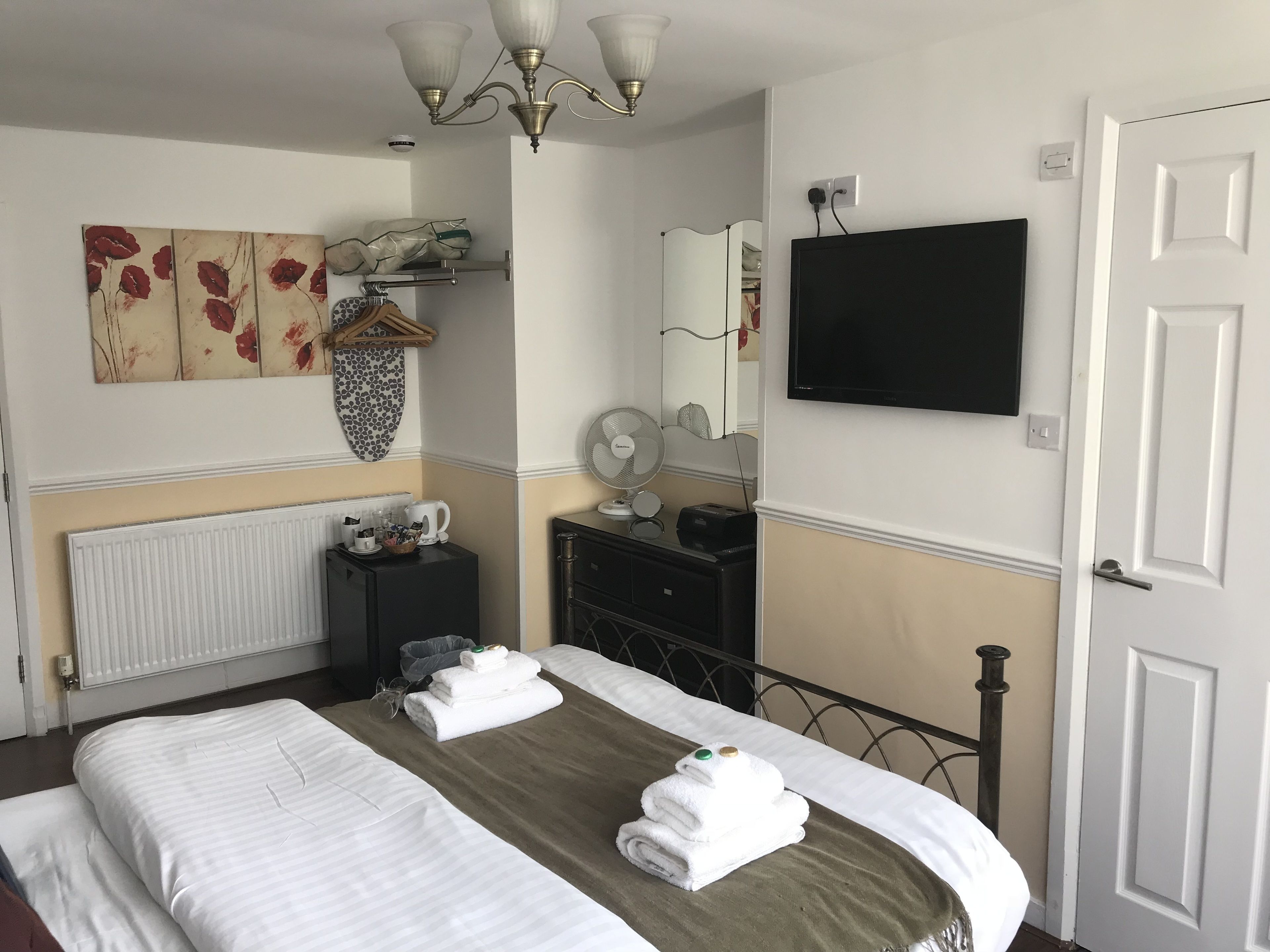 Una habitación de hotel con una cama, un radiador, un ventilador, un espejo y un televisor en la pared.