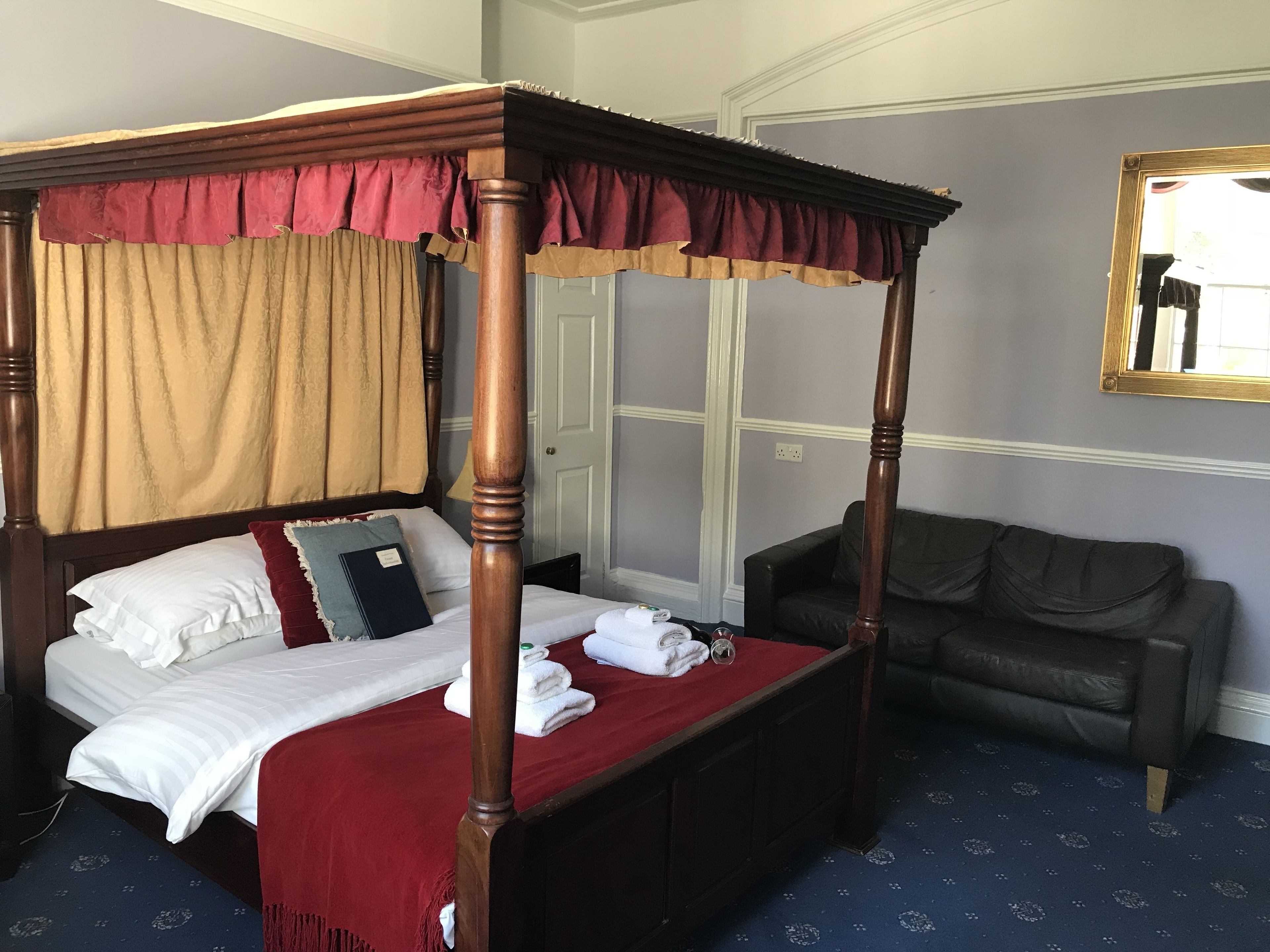 Un letto a baldacchino con tenda rossa, un divano scuro e un tappeto a motivi.