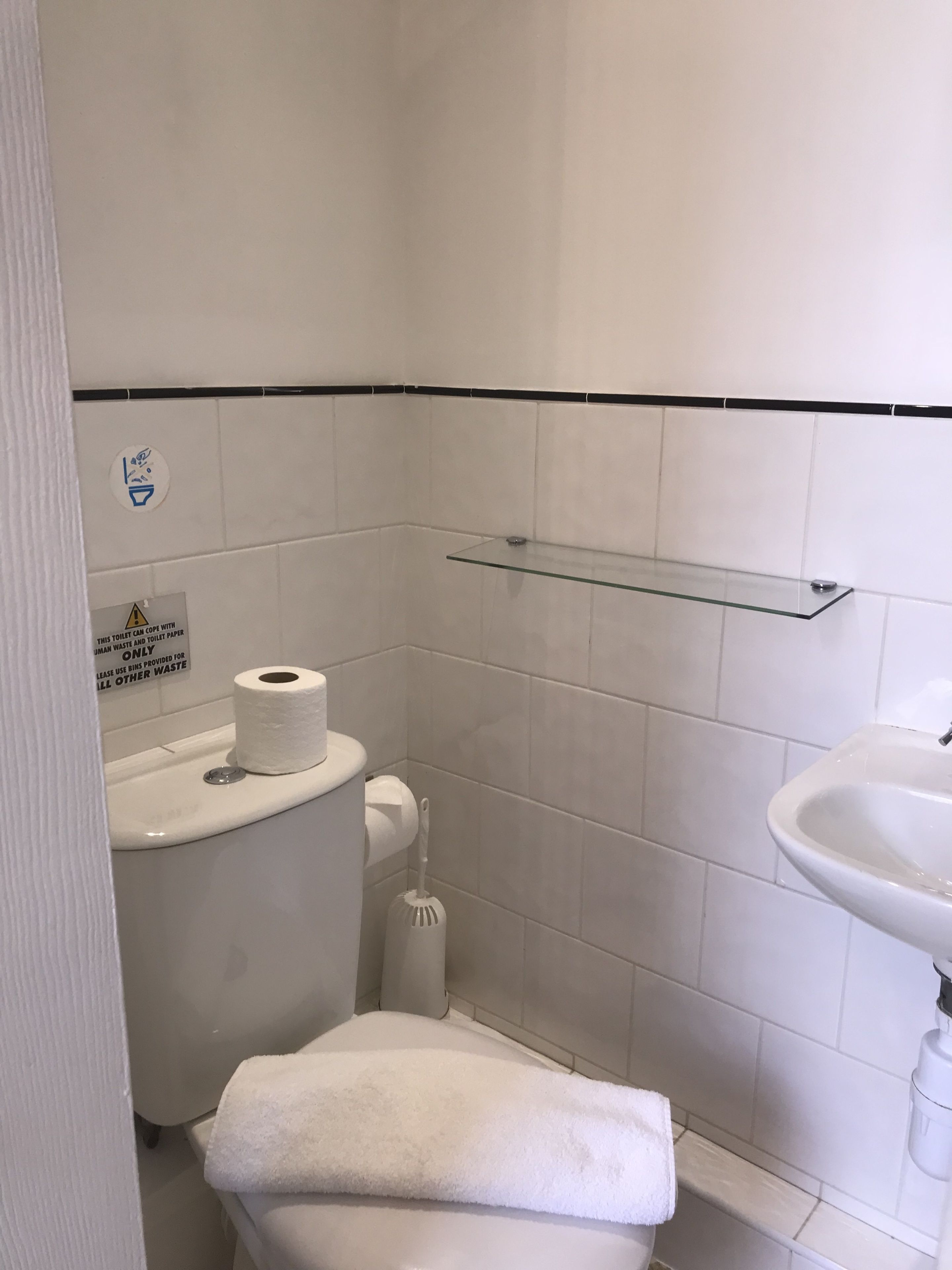 A small, clean bathroom with a toilet, a glass shelf, a sink, and a towel.