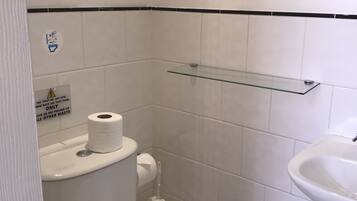 A small, clean bathroom with a toilet, a glass shelf, a sink, and a towel.