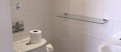Un baño pequeño y limpio con inodoro, repisa de vidrio, lavamanos y toalla.