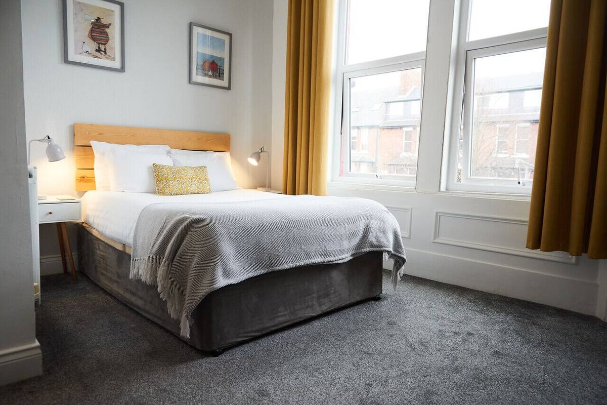 A neatly arranged hotel room with a bed, bedside tables, and a window with curtains.