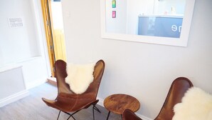 Una habitación con dos sillones de cuero marrón, mantas de piel blanca, una mesita de madera y un espejo grande en la pared.