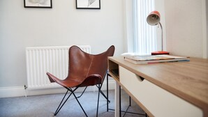 Una habitación con un escritorio de madera, una silla de cuero marrón, un radiador y dos obras de arte con hojas enmarcadas en la pared.