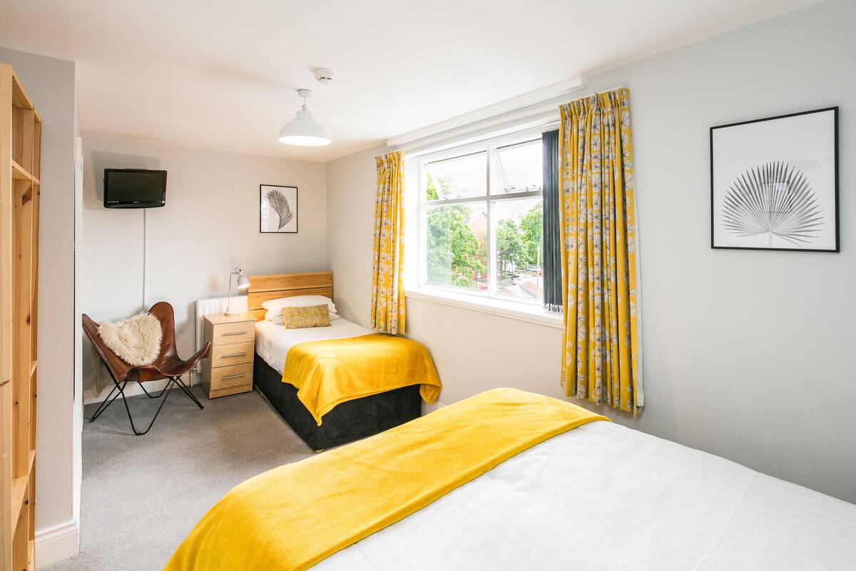 A bedroom with two beds, a chair, a desk, and a window with curtains.