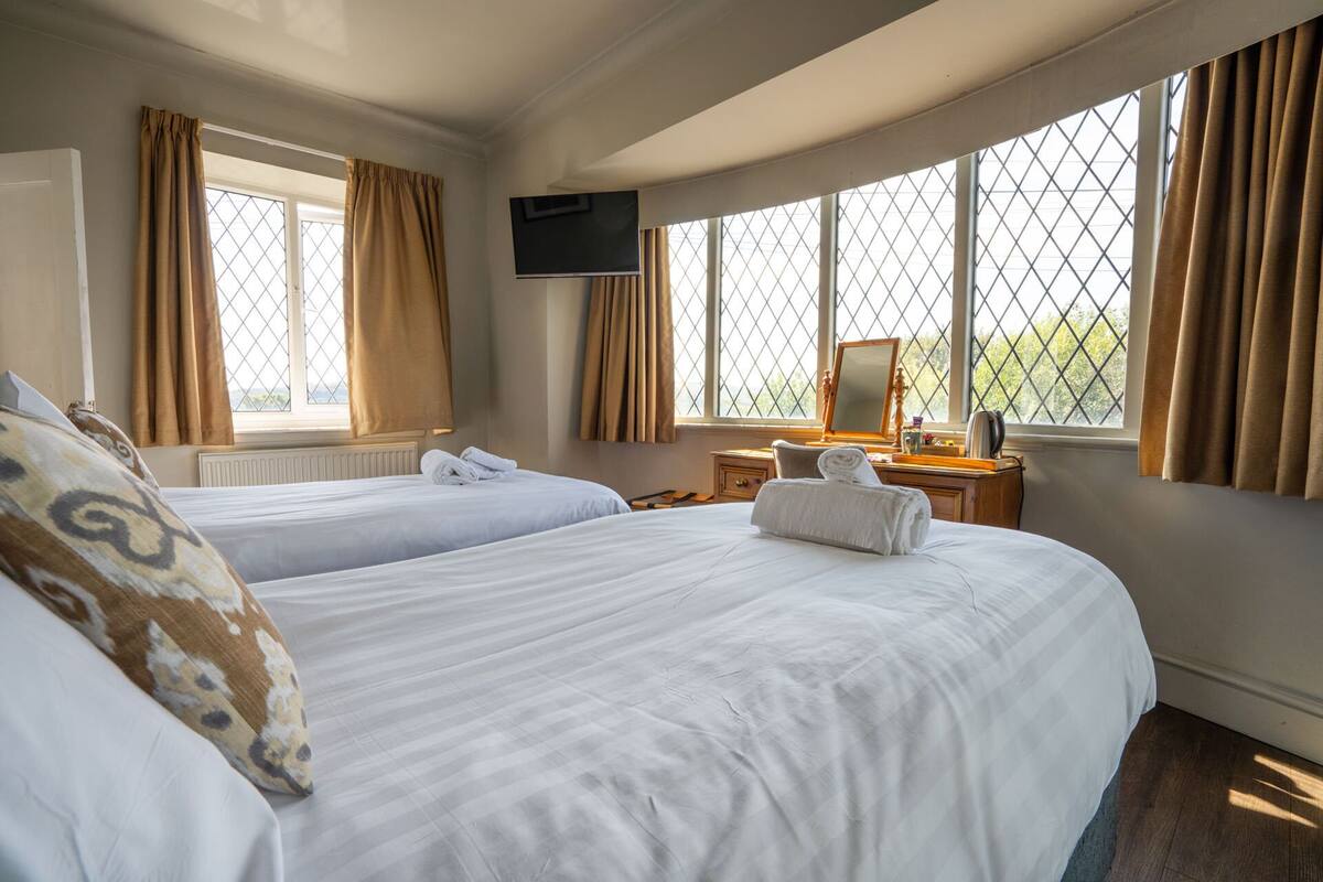 Habitación de hotel con dos camas, televisión, cómoda y ventanas amplias con cortinas.