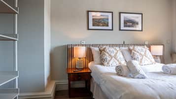 Un dormitorio con una cama, dos lámparas de noche, una mesita de noche, piso de madera y dos cuadros en la pared.