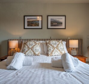 A neatly made bed with patterned pillows, two bedside lamps, and two framed pictures on the wall.