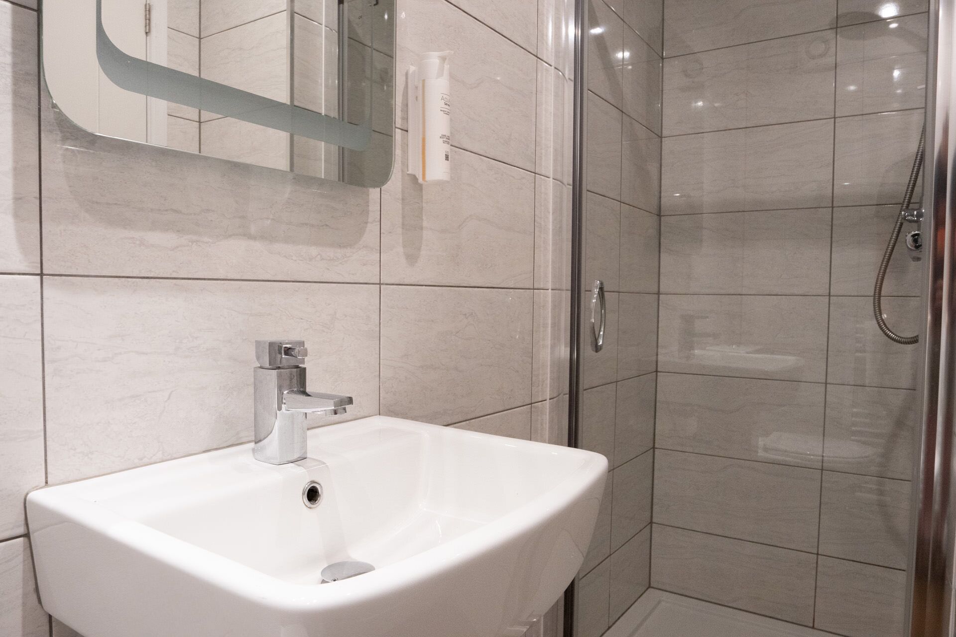 Un baño con lavamanos blanco, espejo y ducha.