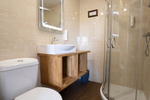 A bathroom with a toilet, sink, wooden vanity, mirror, and glass-enclosed shower.