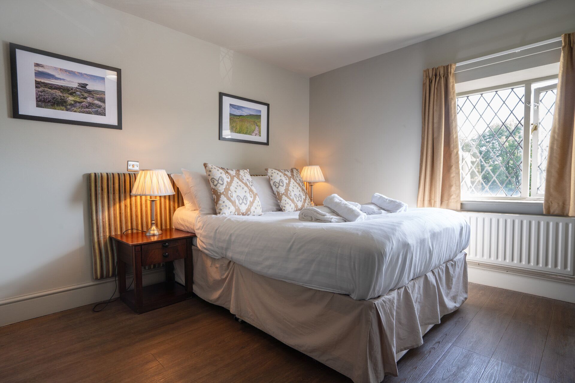 A neatly arranged bedroom with a bed, two bedside lamps, a nightstand, and a window with curtains.