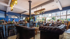 Un restaurant chaleureux, avec des meubles en bois, de grandes fenêtres et des plantes suspendues.