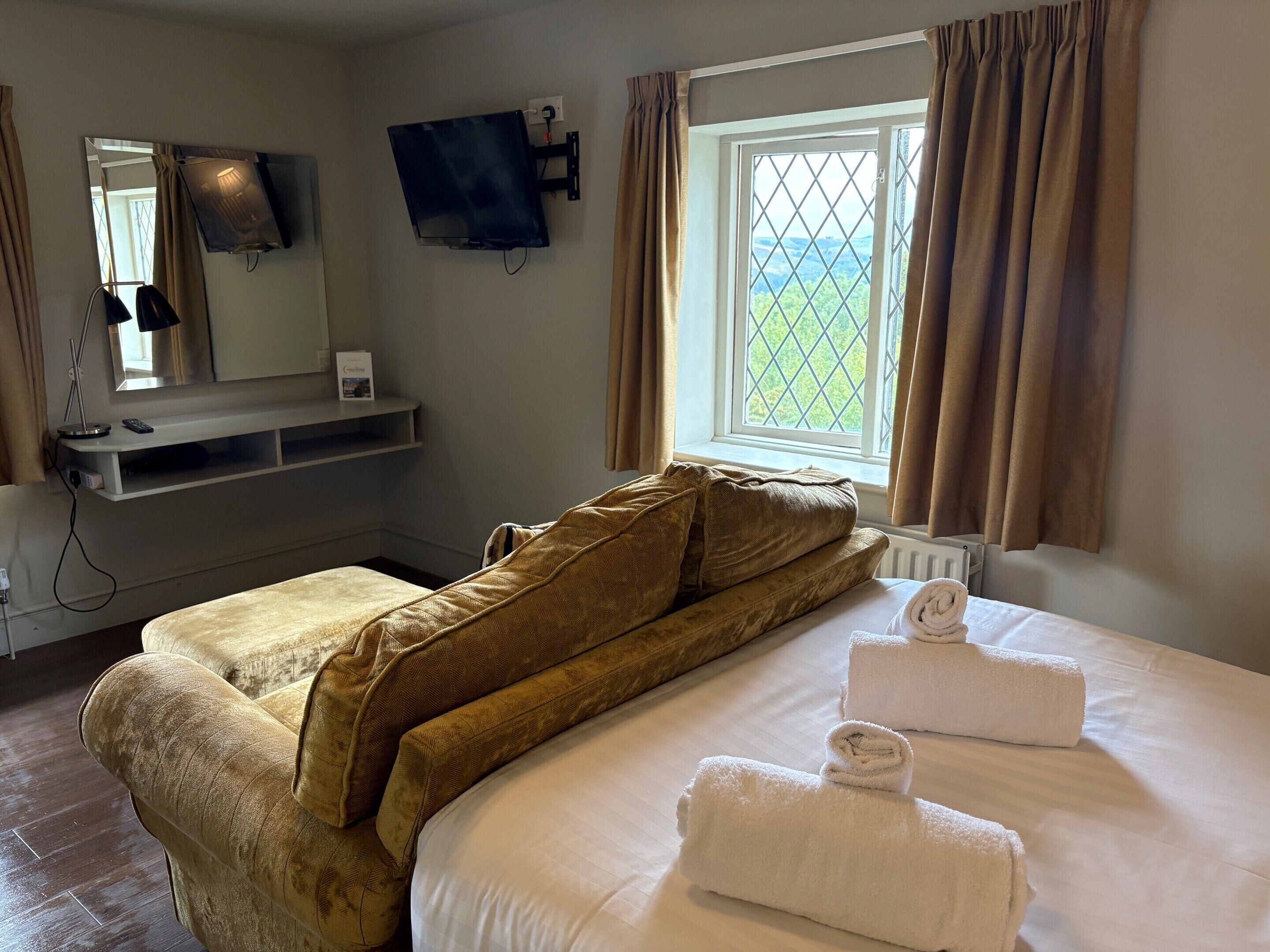 A hotel room with a bed, a TV mounted on the wall, a window with curtains, and a view of the outdoors.