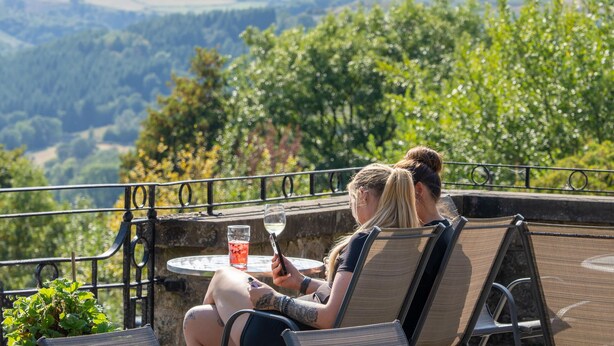 Deux personnes sont assises à une table, un verre à la main, et contemplent un paysage magnifique.
