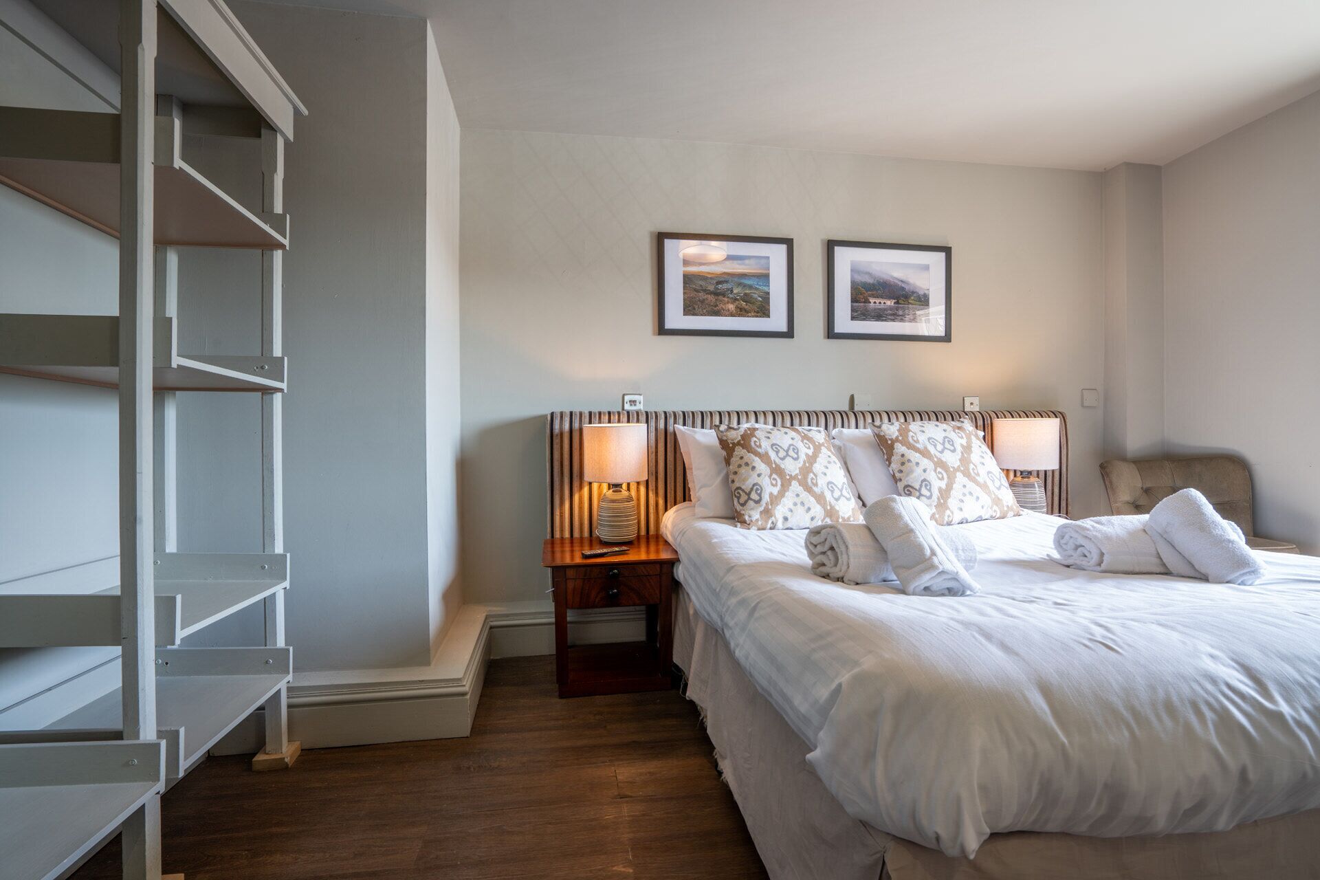 A hotel room with a bed, two bedside lamps, a nightstand, a wardrobe, and two framed pictures on the wall.