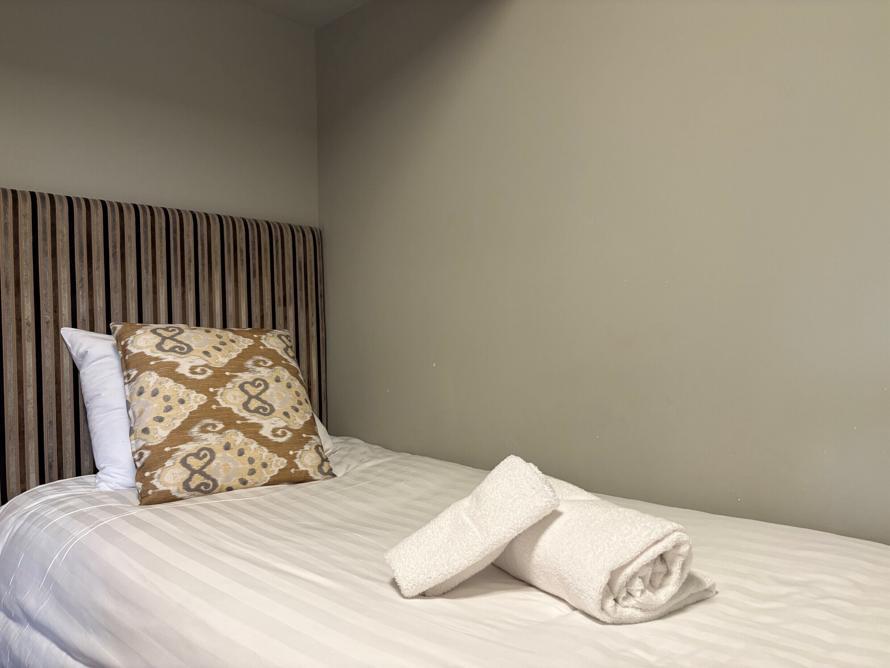 A neatly made bed with a striped headboard, a patterned pillow, and a rolled white towel.