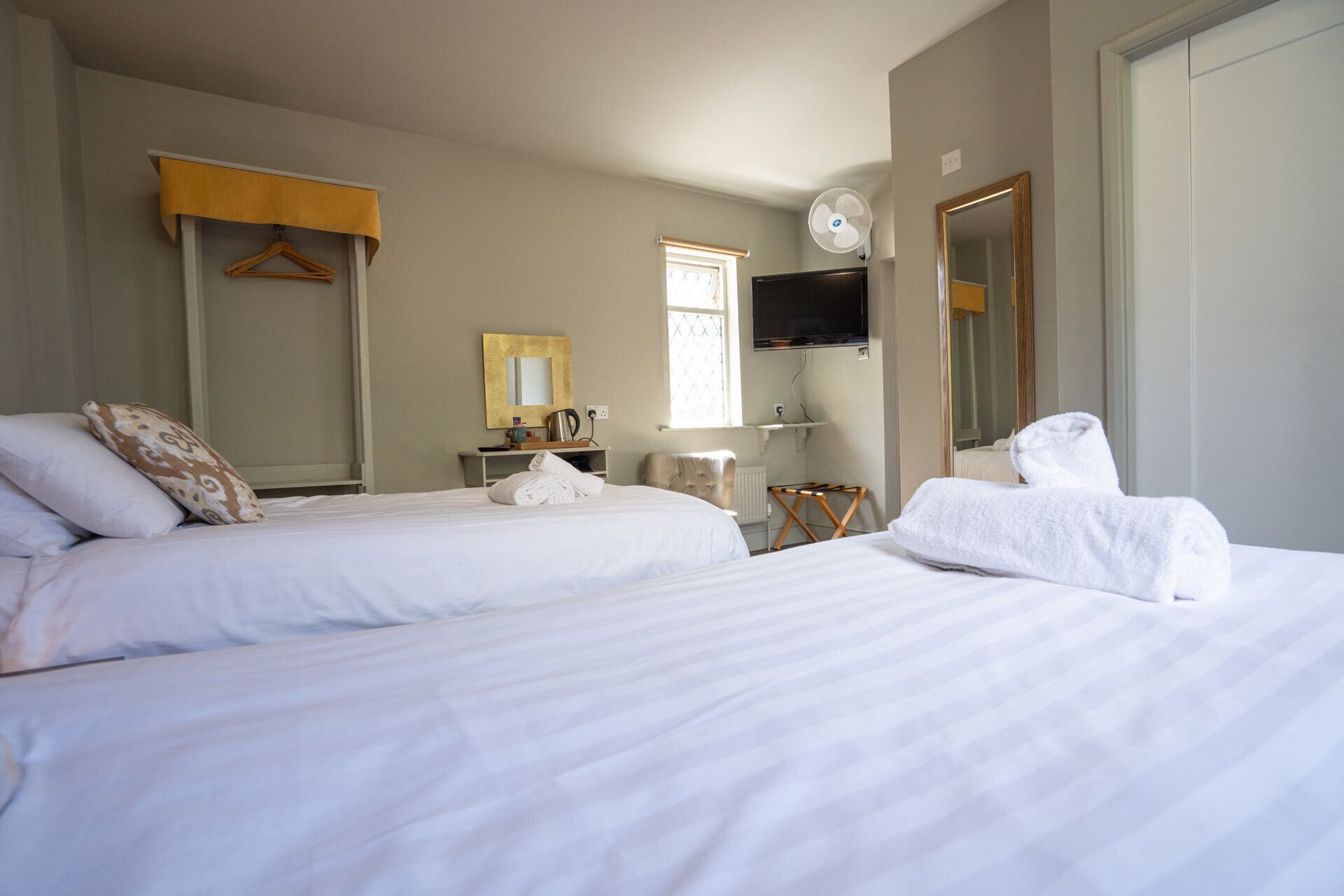 Habitación de hotel con dos camas, televisor, espejo, ventana y perchero para toallas.