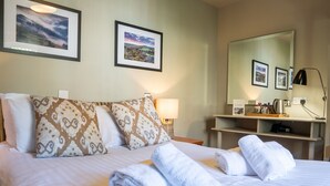 Une chambre d’hôtel comprenant un lit, des oreillers, une table de chevet avec une lampe, un miroir et des serviettes.