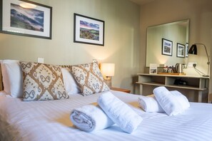 Una habitación de hotel con cama, almohadas, mesita de noche con lámpara, espejo y toallas.