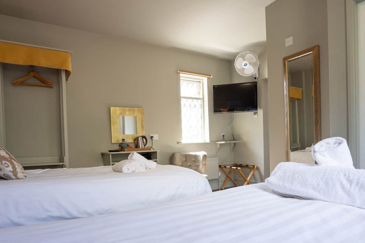 Habitación de hotel con dos camas, televisión, espejo, radiador y una pequeña mesa con una tetera.