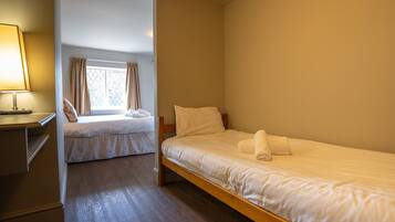 Un dormitorio con dos camas, una ventana con cortinas, una mesita de noche con lámpara y suelo de madera.