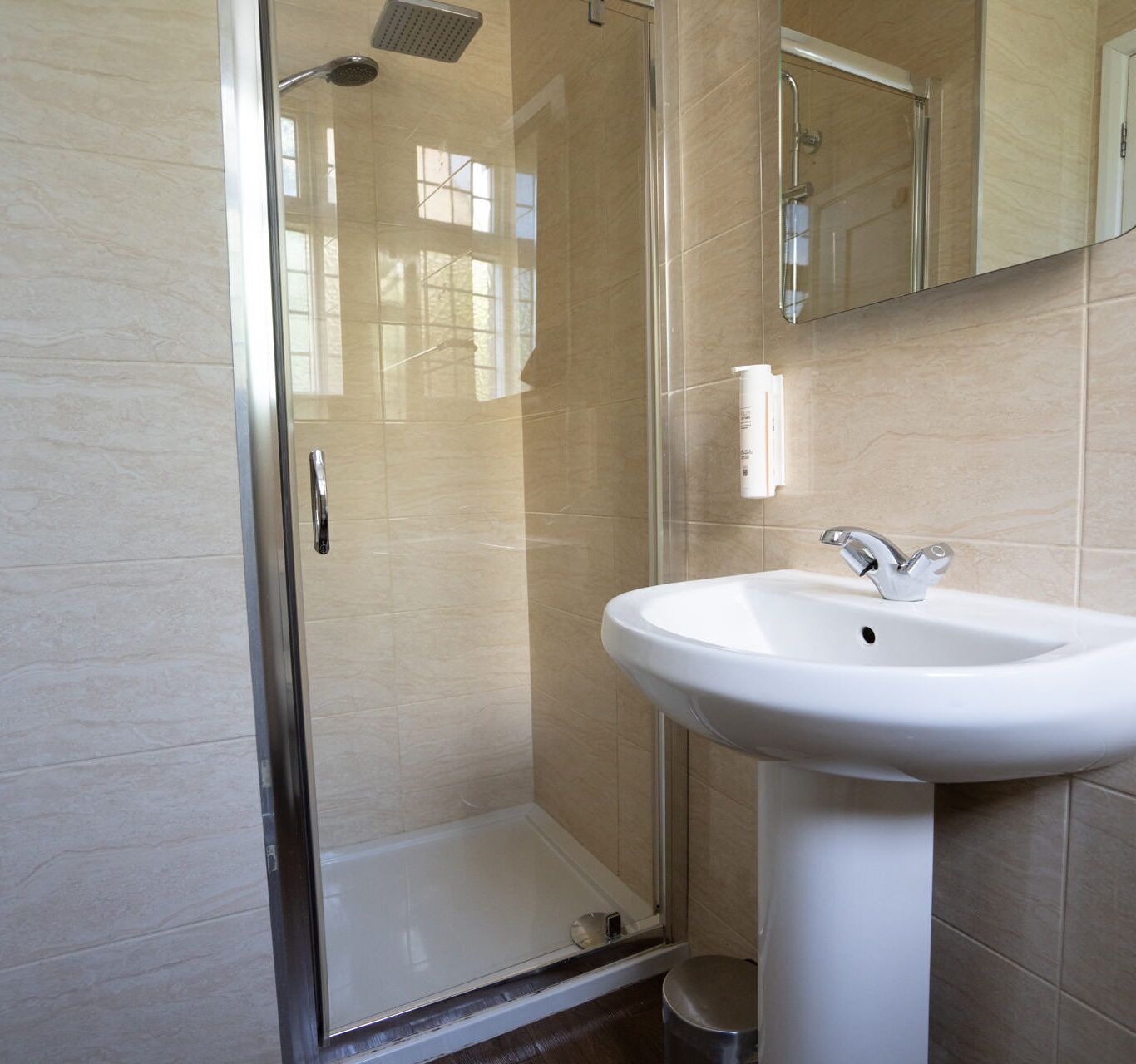A bathroom with a glass-enclosed shower, a white sink, and a mirror.