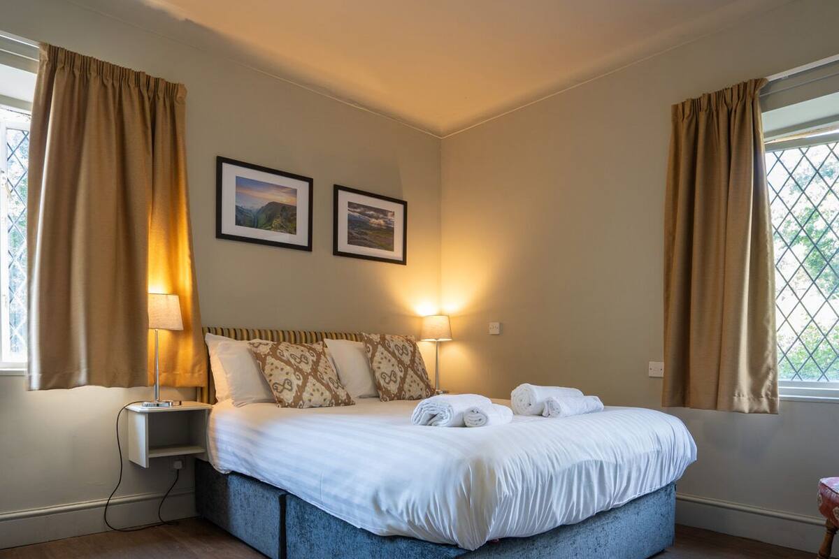 Un dormitorio con una cama, lámparas de noche, una silla y dos cuadros en la pared.