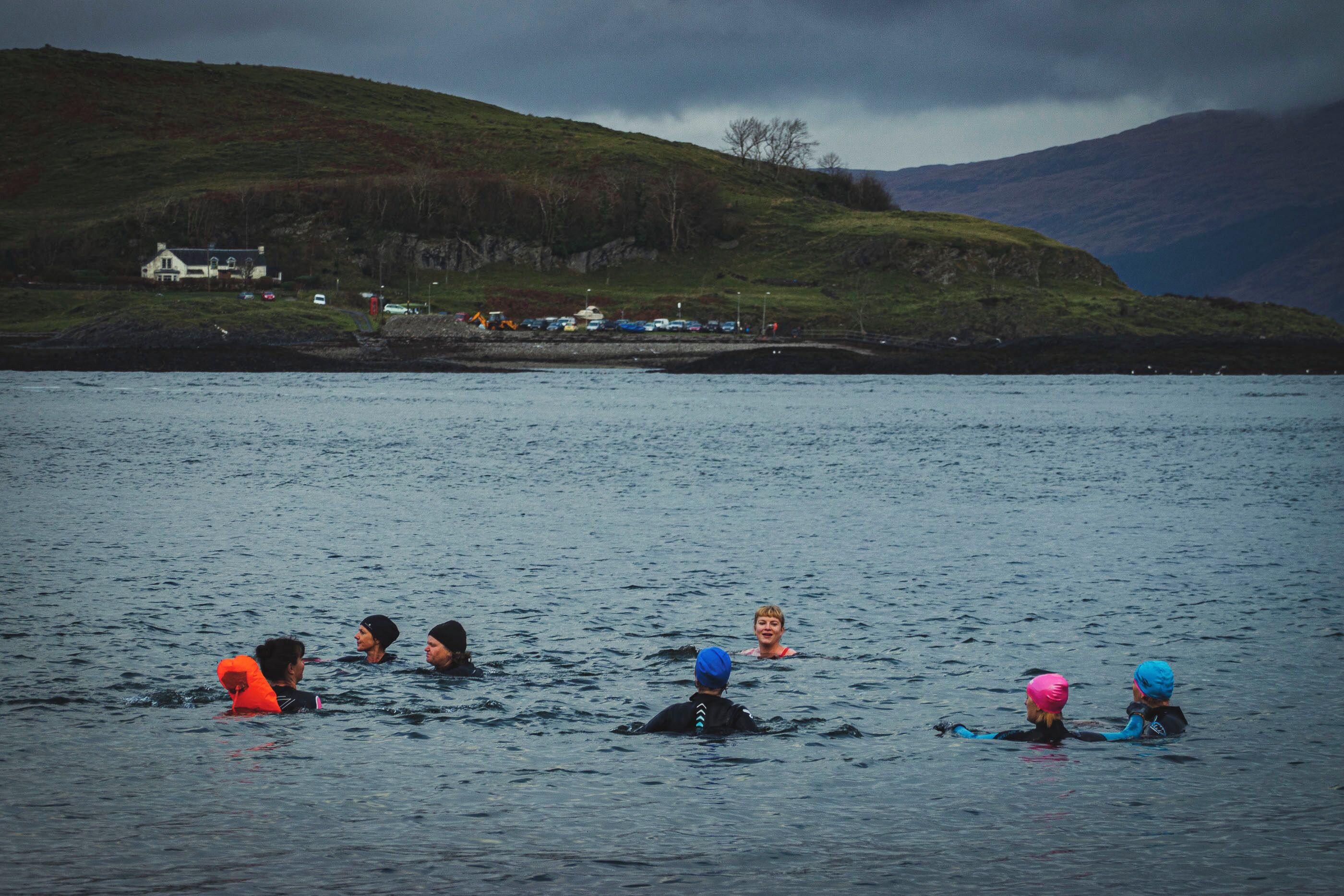 A group of people swimming in a body of water with a hilly landscape in the background.