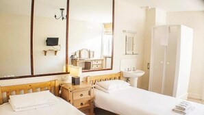 A hotel room with two single beds, a wooden dresser, a large mirror, a wardrobe, a bedside table with a lamp, and a window.