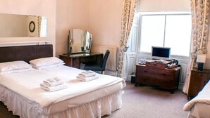 A hotel room with a large bed, a desk with a computer, a chair, and a dresser.