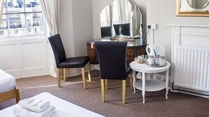 A hotel room with a bed, a desk with a chair, a small table with a kettle, and a mirror on the wall.