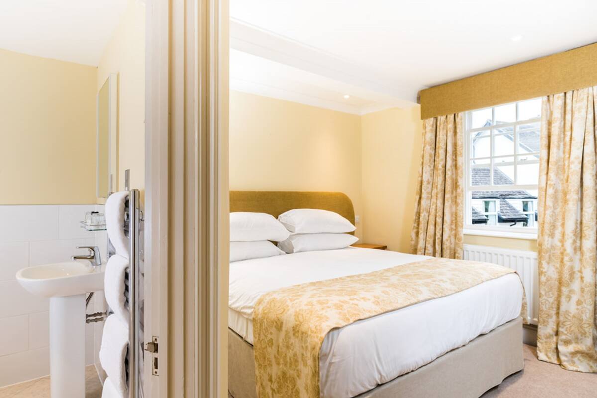 Une chambre d’hôtel comprenant un lit, une table de chevet, une fenêtre avec des rideaux et une salle de bain avec un lavabo et un miroir.