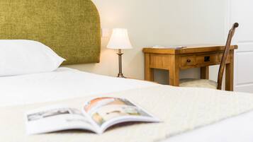 Una cama bien tendida con una revista encima, una lámpara de noche, una mesita de madera y una silla.