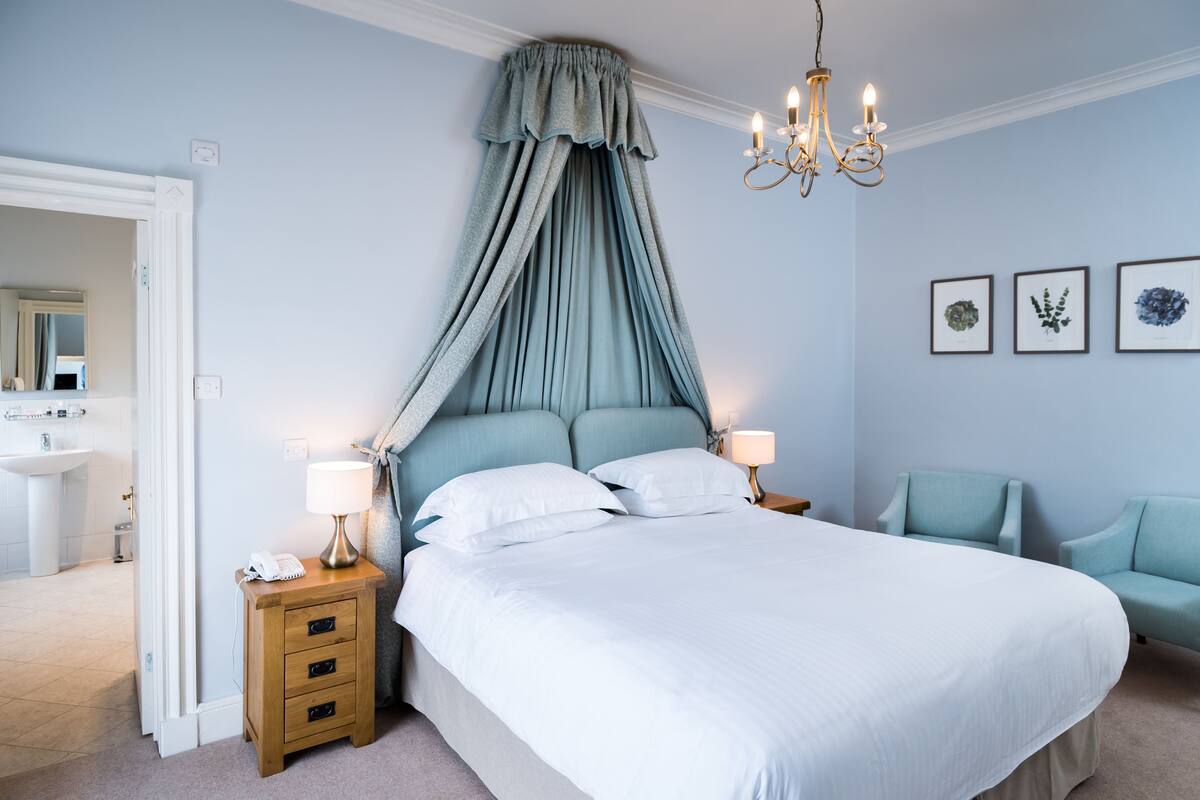 Une chambre à coucher avec un grand lit, des lampes de chevet, une table de chevet, une chaise et un lustre.