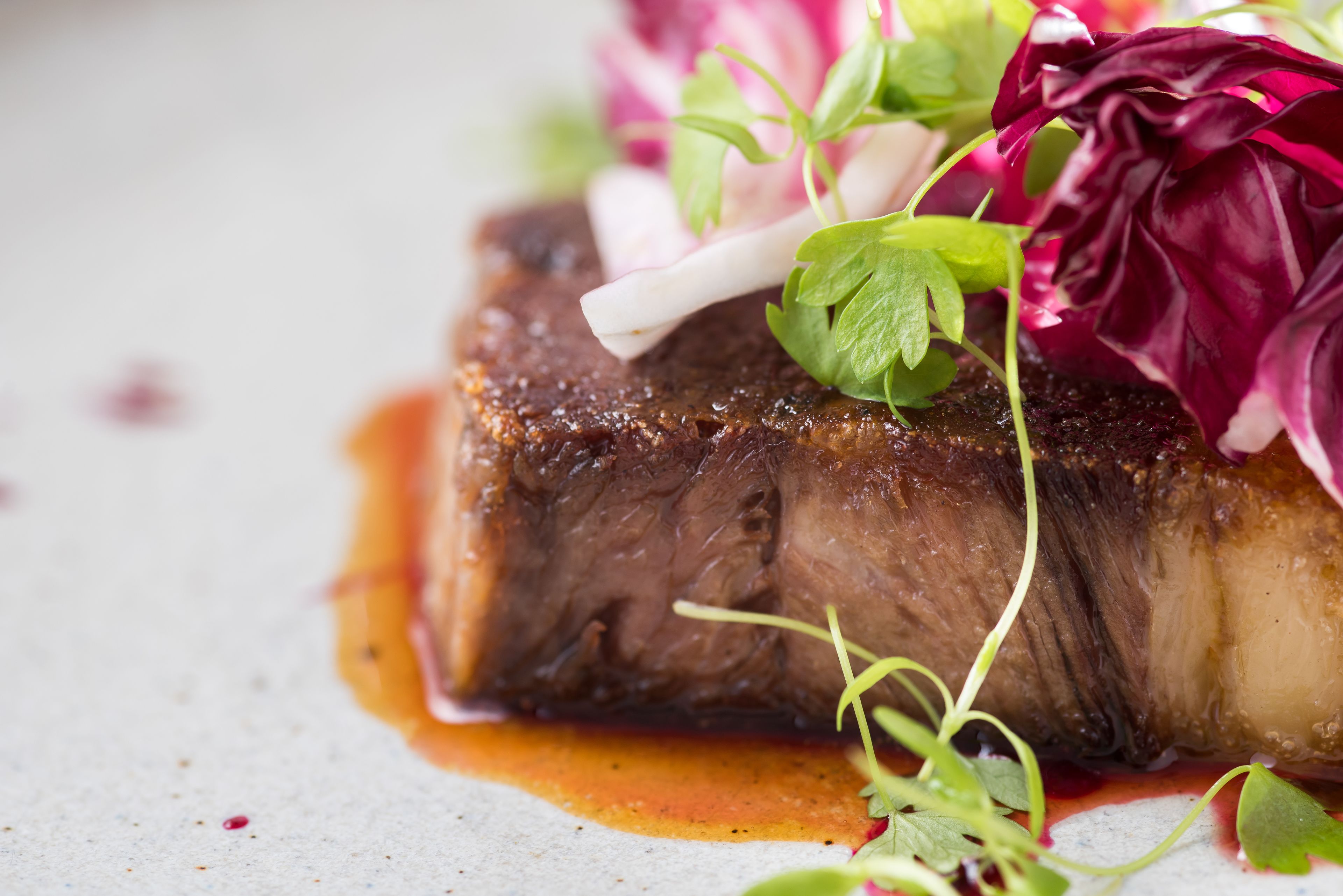 A close-up of a cooked steak with a sauce and garnishes.