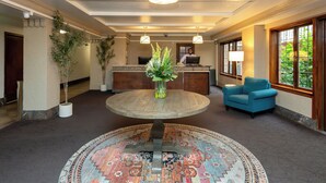 A lobby with a round wooden table, a reception desk, a blue armchair, and a patterned rug. - The Inn at Virginia Mason (Seattle)