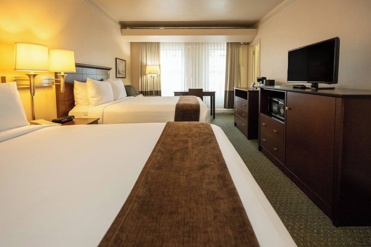 A hotel room with two beds, a TV, a desk, and a dresser.