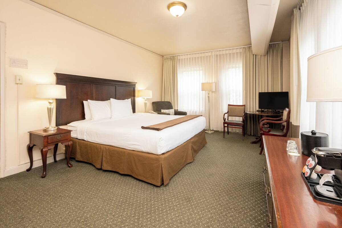A hotel room with a large bed, a desk with a coffee maker, a TV, and a chair.
