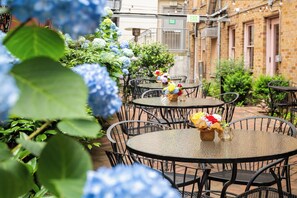 A courtyard with round tables and chairs, surrounded by greenery and flowers.