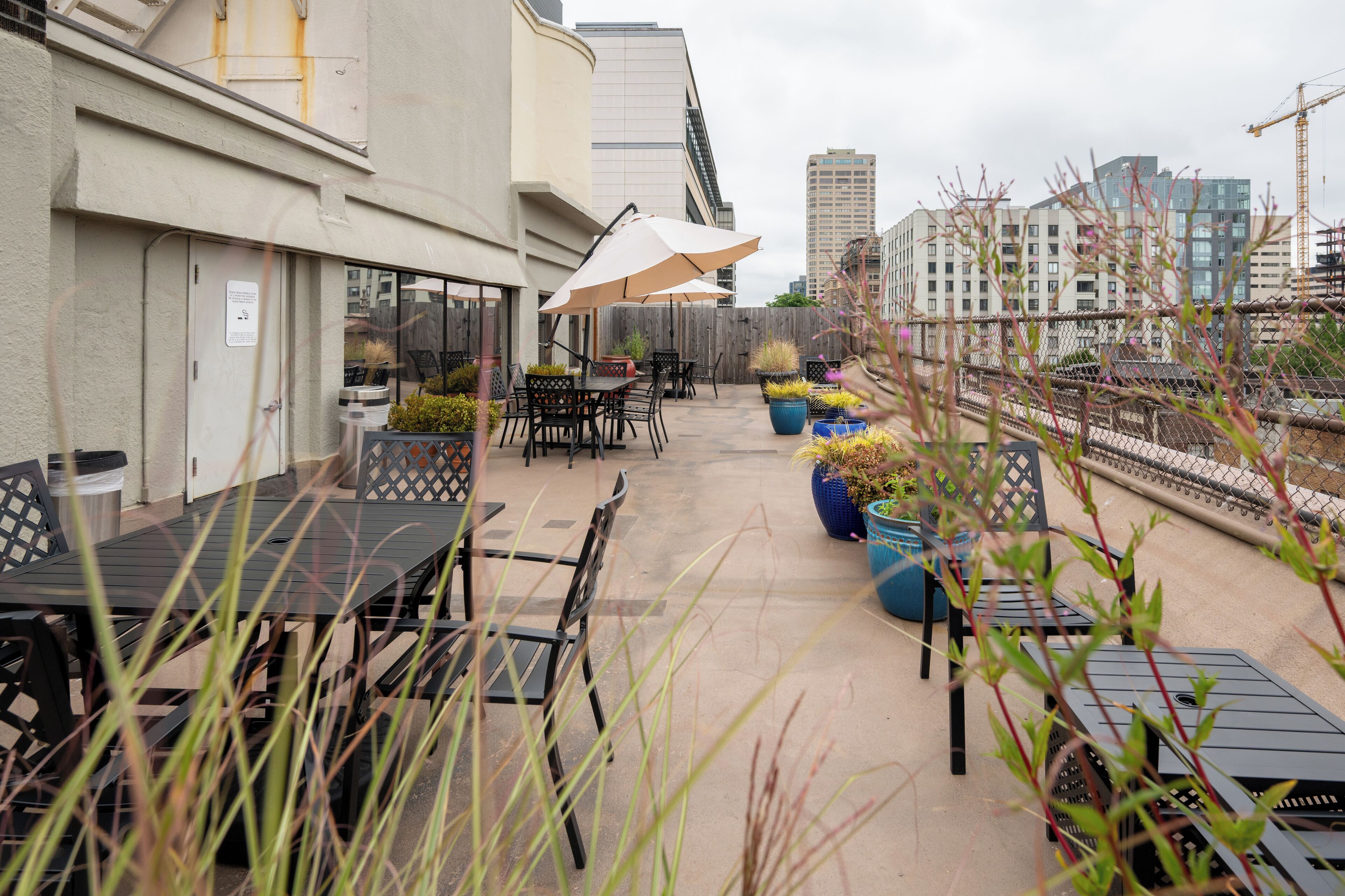 An outdoor patio area with tables and chairs, potted plants, and a view of the cityscape.