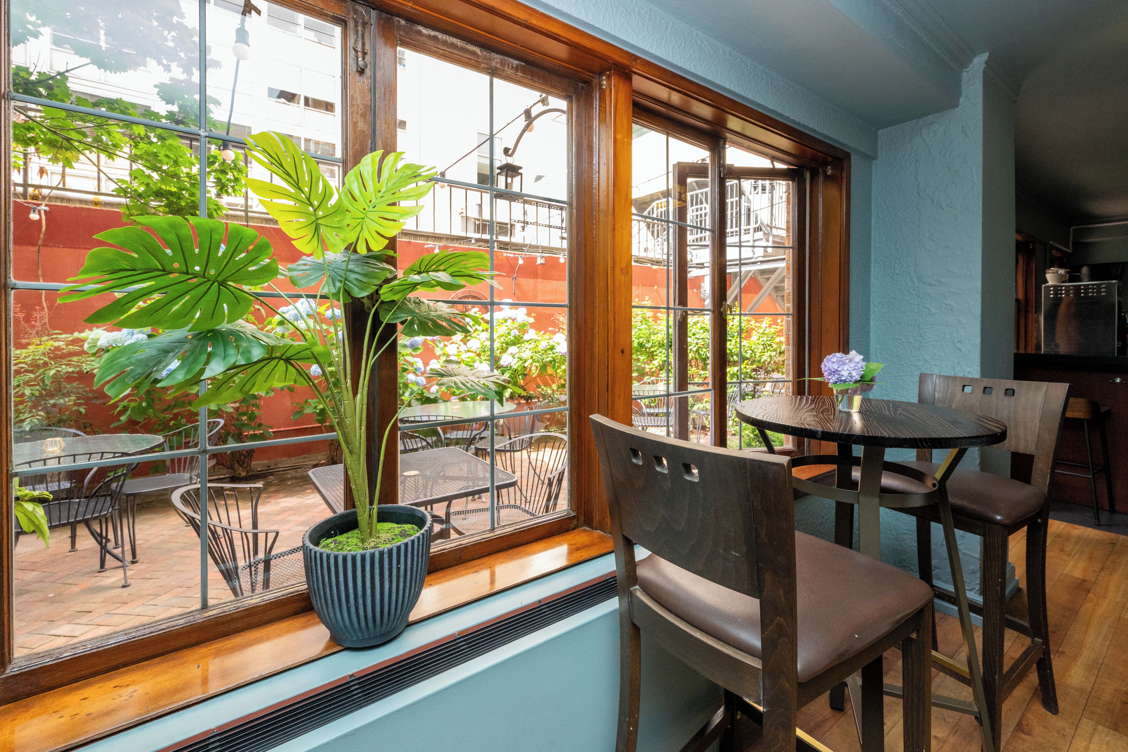 Un comedor con un ventanal grande, una planta en maceta y una mesa con sillas.