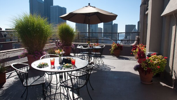 A rooftop terrace with outdoor seating, potted plants, and a view of city buildings. - The Inn at Virginia Mason (Seattle)