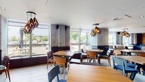 Un restaurant spacieux avec des tables et des chaises en bois, de grandes fenêtres et un éclairage moderne à suspension.