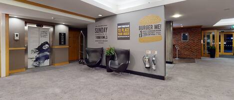 Zona de recepción de hotel con diseño moderno, que incluye un mostrador de recepción, área de descanso y una pared con carteles promocionales.