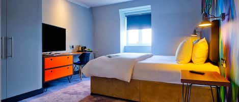 A bedroom with a bed, a desk, a chair, a TV, and a window.