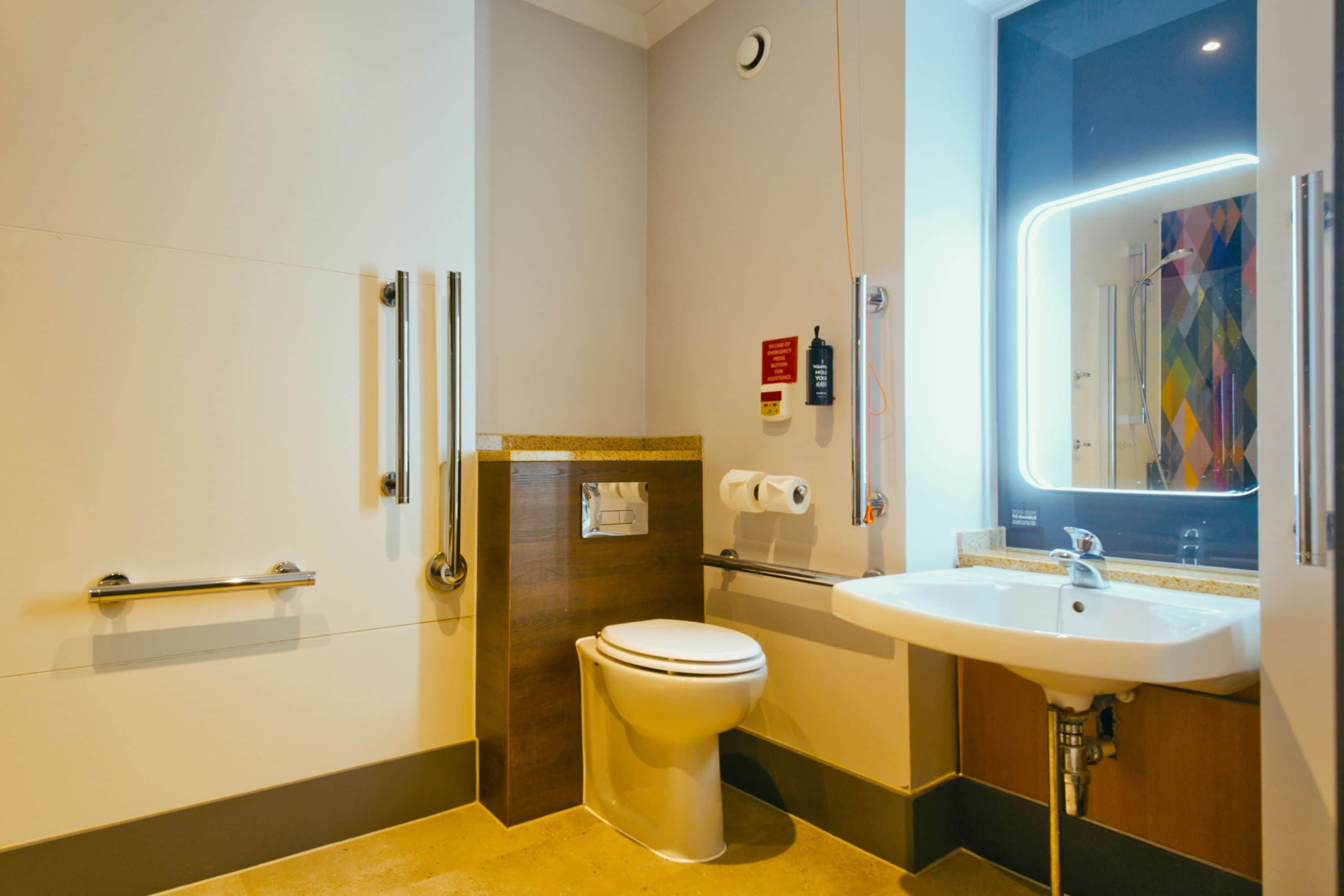 Un baño moderno con inodoro, lavamanos y barras de apoyo.